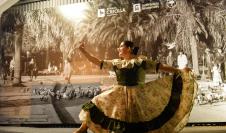 Mujer con vestido tradicional, bailando detrás hay un logo de la semana criolla