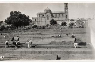 Preparación del terreno para las franjas de cimentación. Al fondo, la Iglesia de Nuestra Señora de los Dolores, más conocida como Tierra Santa. Enero de 1921. Toma directa.