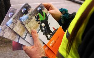 Conductor con chaleco sosteniendo varios manuales iguales con el título "Motos cómo viajar seguros"