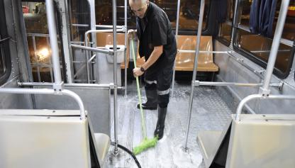 Hombre trabajador del transporte con escoba en mano, lavando con una manguera el piso del ómnibus.