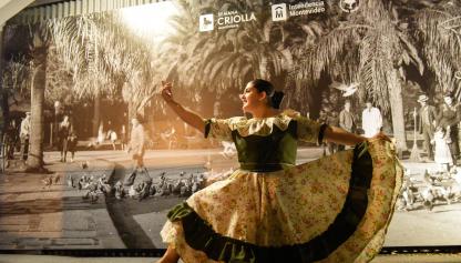 Mujer con vestido tradicional, bailando detrás hay un logo de la semana criolla