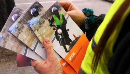 Conductor con chaleco sosteniendo varios manuales iguales con el título "Motos cómo viajar seguros"