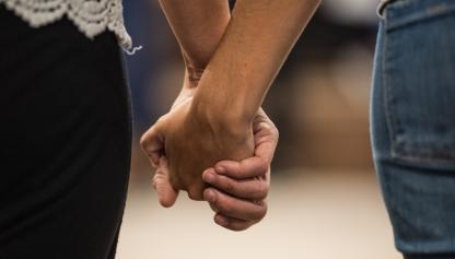 Una mujer y un hombre de espaldas tomados de la mano. Se destacan las manos y antebrazo de ambos.